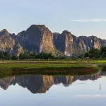 Vang Vieng travel guide — limestone karst peaks reflected in flooded paddy water at golden hour beside the Nam Song