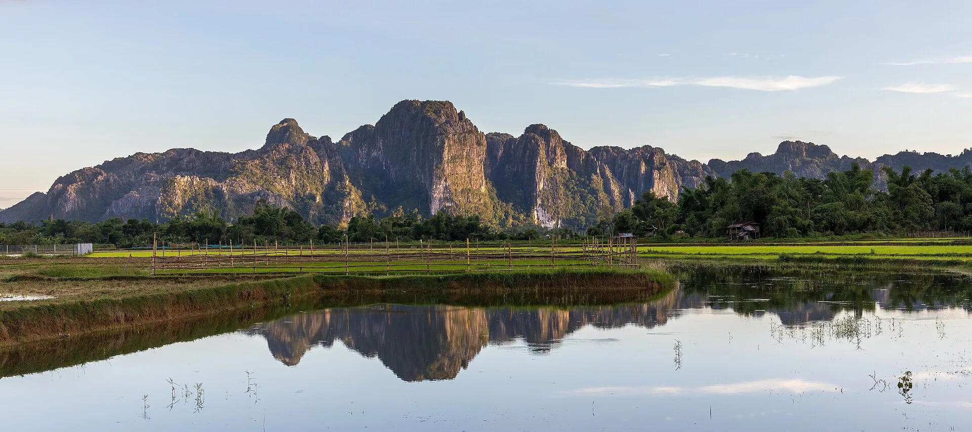 Vang Vieng travel guide — limestone karst peaks reflected in flooded paddy water at golden hour beside the Nam Song
