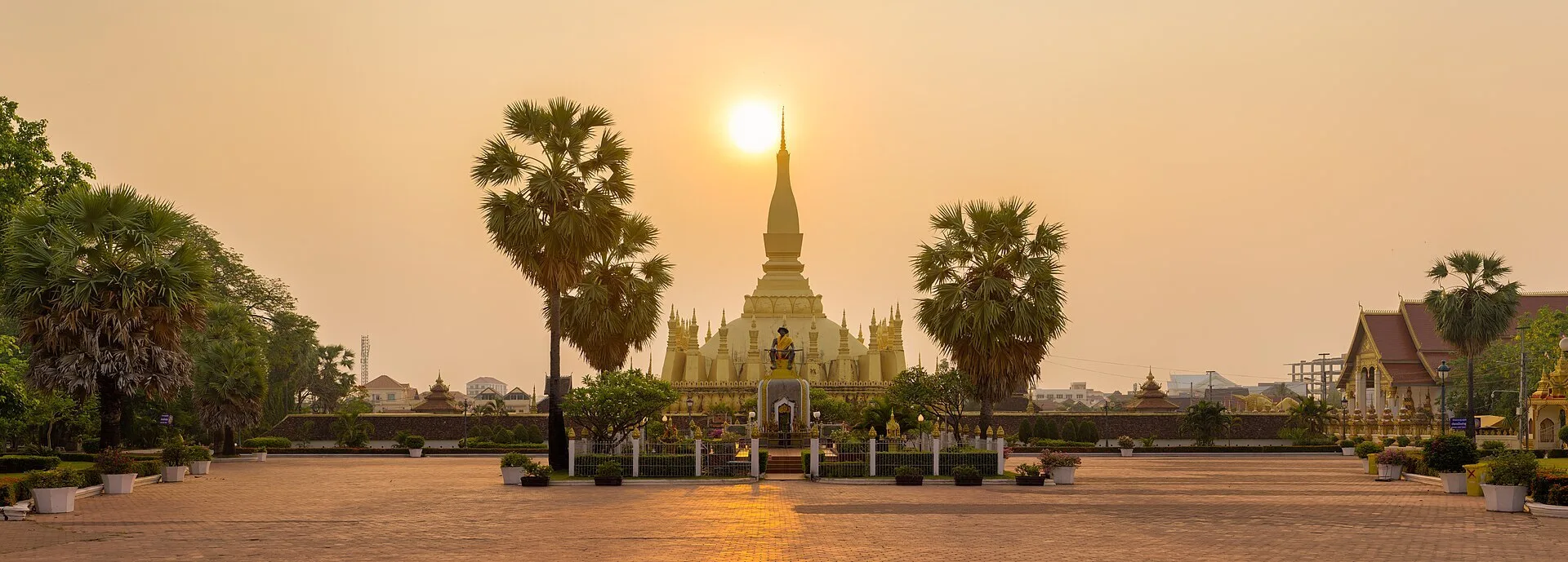 Vientiane travel guide: the golden Pha That Luang stupa glowing at sunset behind palm trees