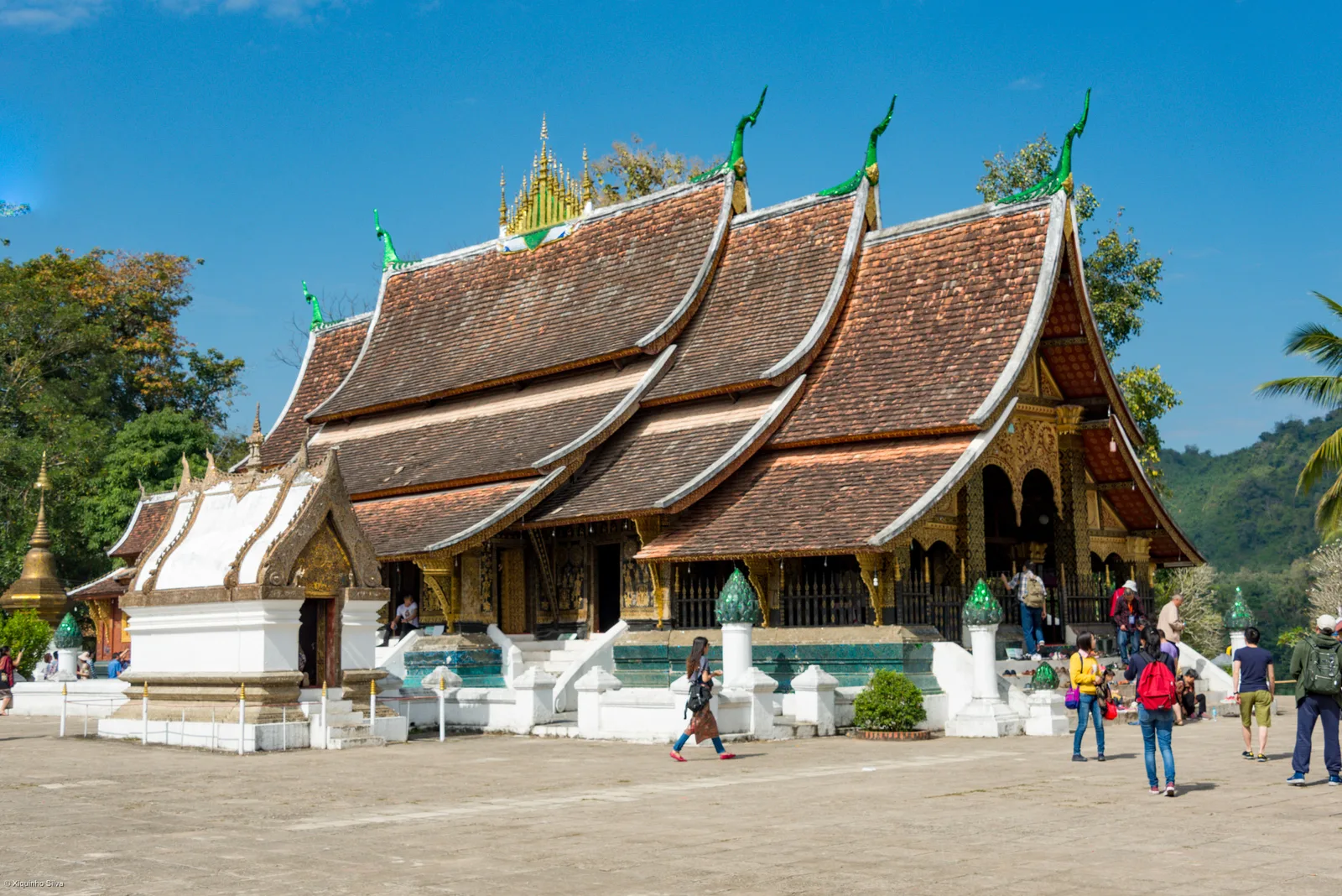 Sweeping low tiered roofs of Wat Xieng Thong temple under blue sky in Luang Prabang
