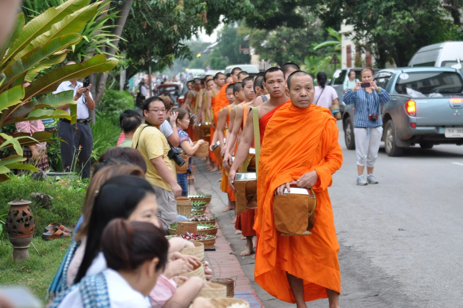 Buddhist monks in orange robes collecting morning alms from kneeling locals during Tak Bat in Luang Prabang