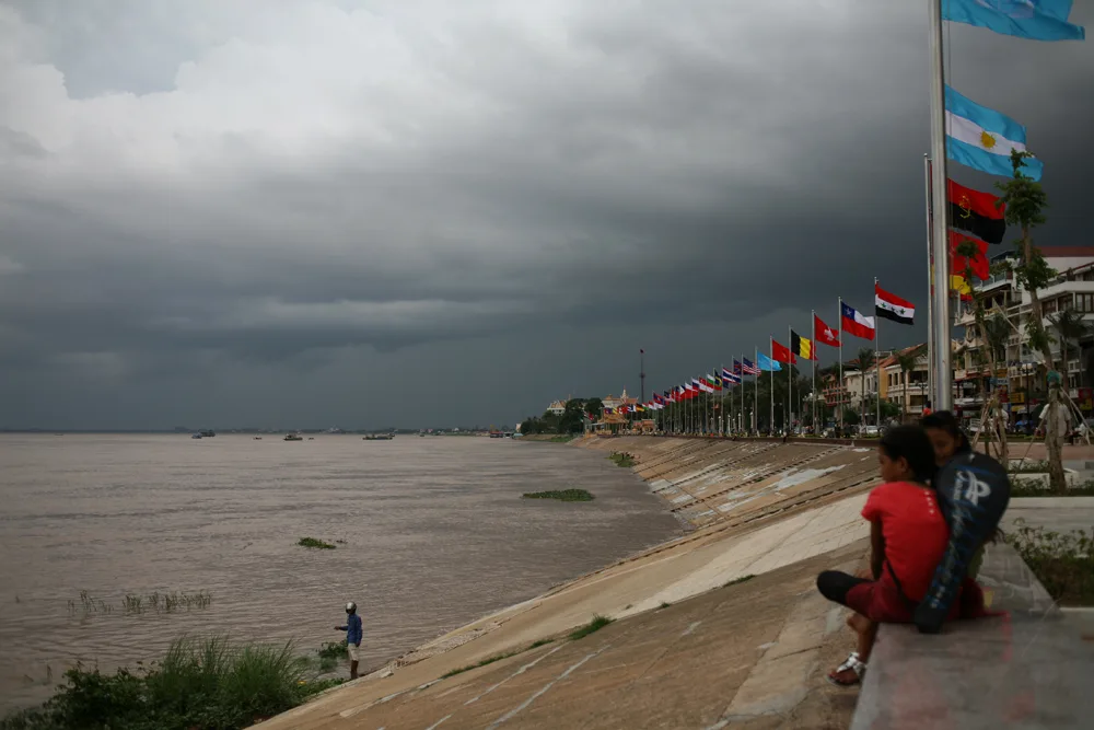 Sisowath Quay riverside promenade in Phnom Penh with a row of international flags and storm clouds over the Tonle Sap river