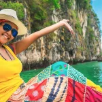 Smiling female traveller in a sun hat on a longtail boat among Phuket's limestone karst cliffs and turquoise water, Thailand