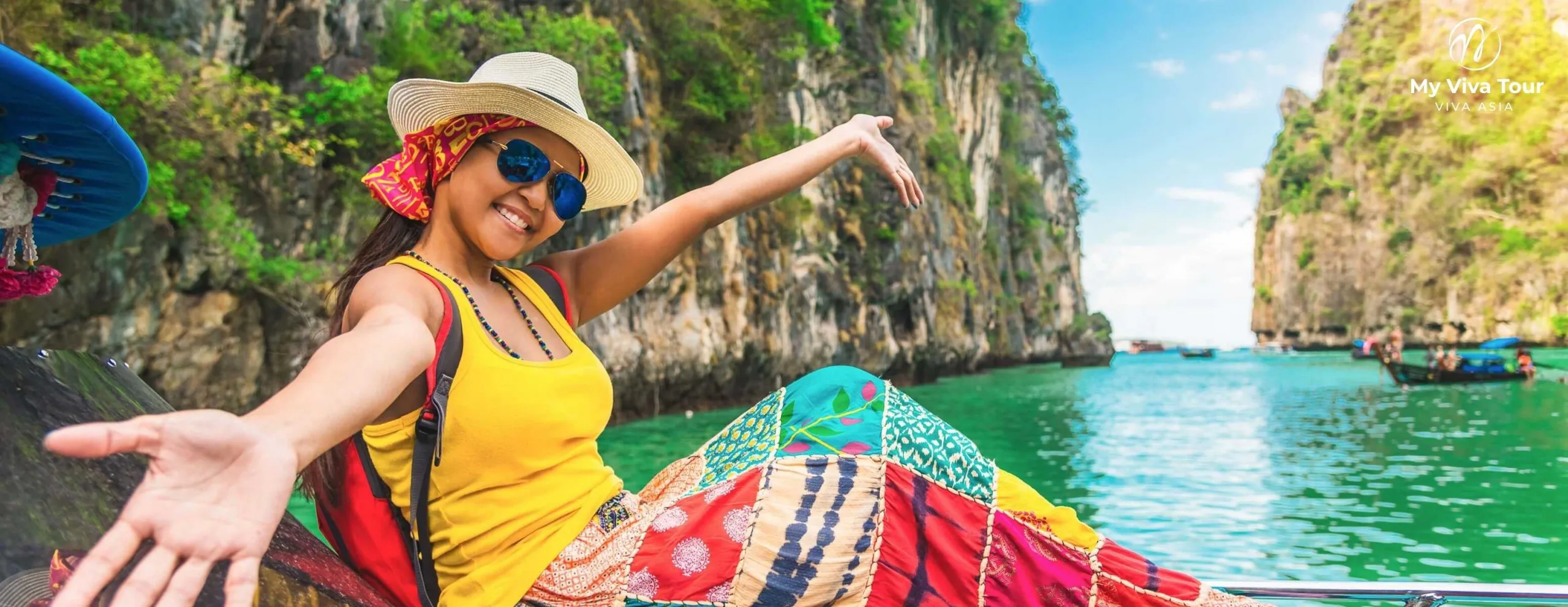 Smiling female traveller in a sun hat on a longtail boat among Phuket's limestone karst cliffs and turquoise water, Thailand