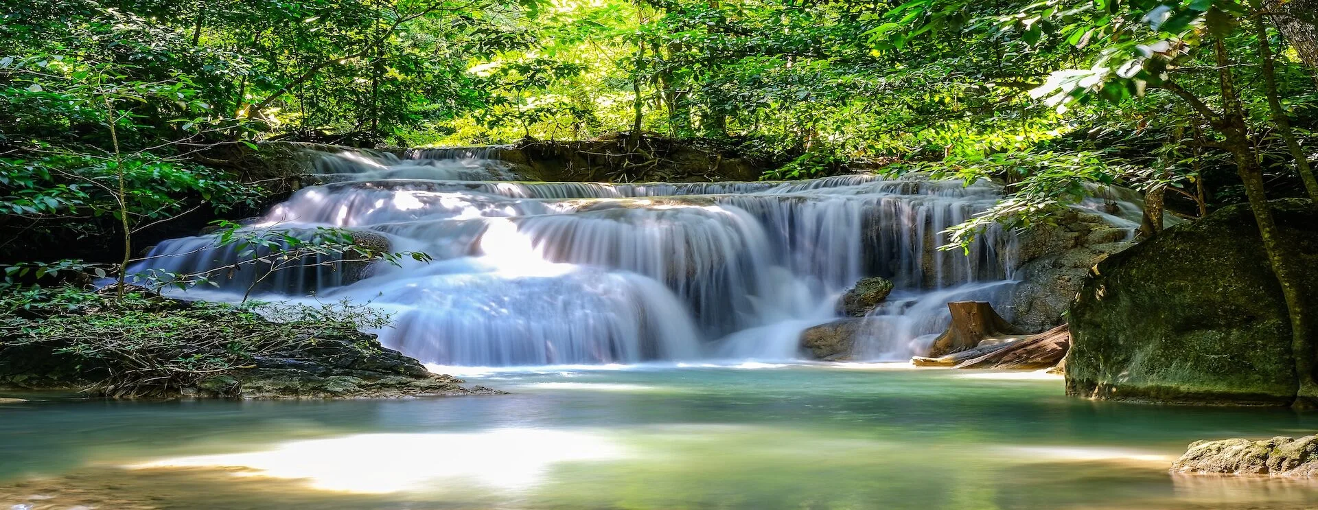 A tiered jungle waterfall tumbling into a calm emerald pool in tropical Thailand