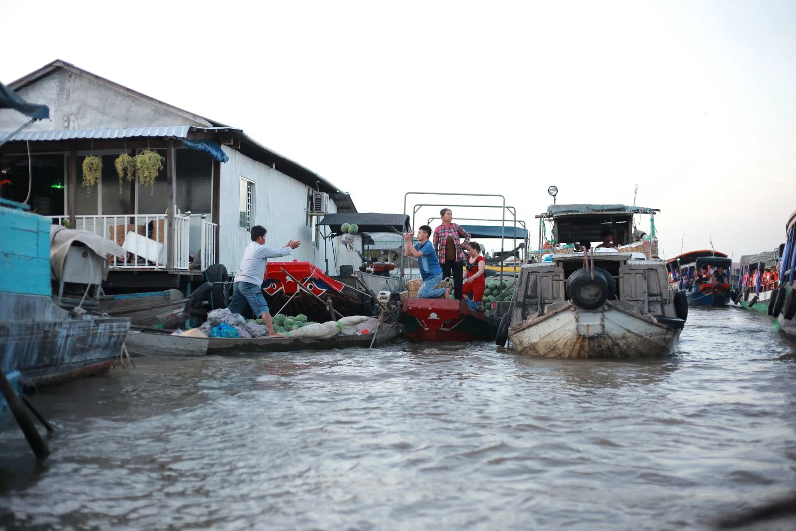 Locals passing watermelons between wooden boats at Can Tho floating market at dawn