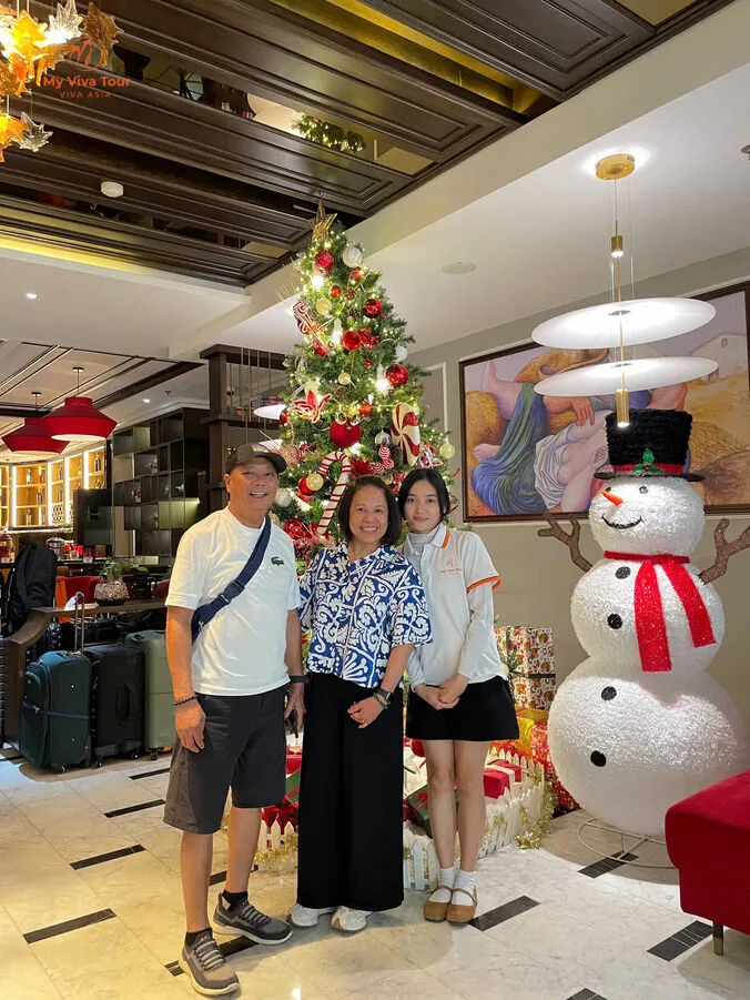 Edward and his wife with their My Viva Tour guide beside a festive Christmas tree in Vietnam