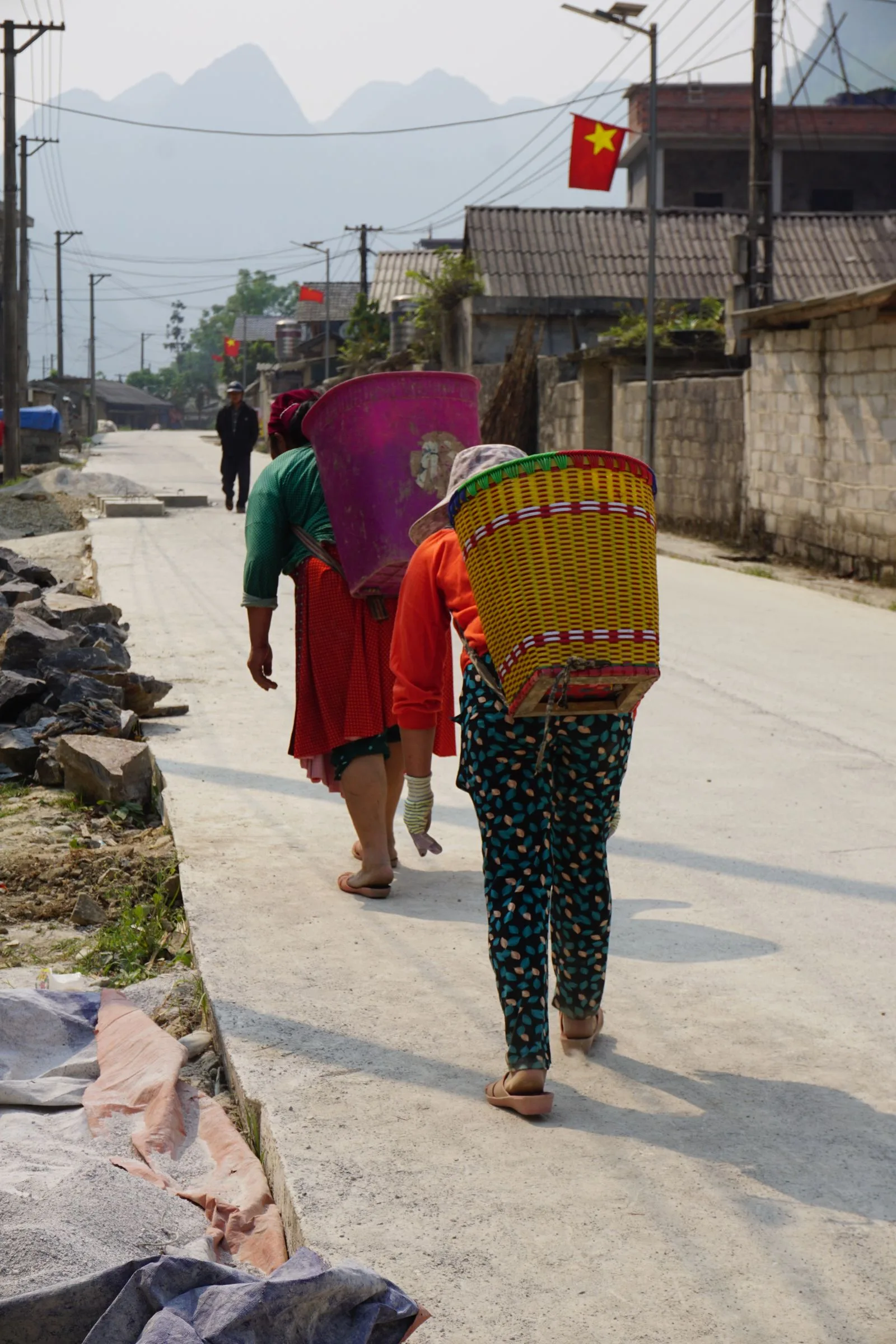 Ethnic minority women carrying woven back-baskets along a village road in Ha Giang