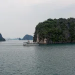 Tour boat passing a forested limestone island on Ha Long Bay, Vietnam