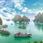 Wooden junk boats cruising between towering limestone karst islands on the emerald water of Ha Long Bay, a highlight of Vietnam private tours