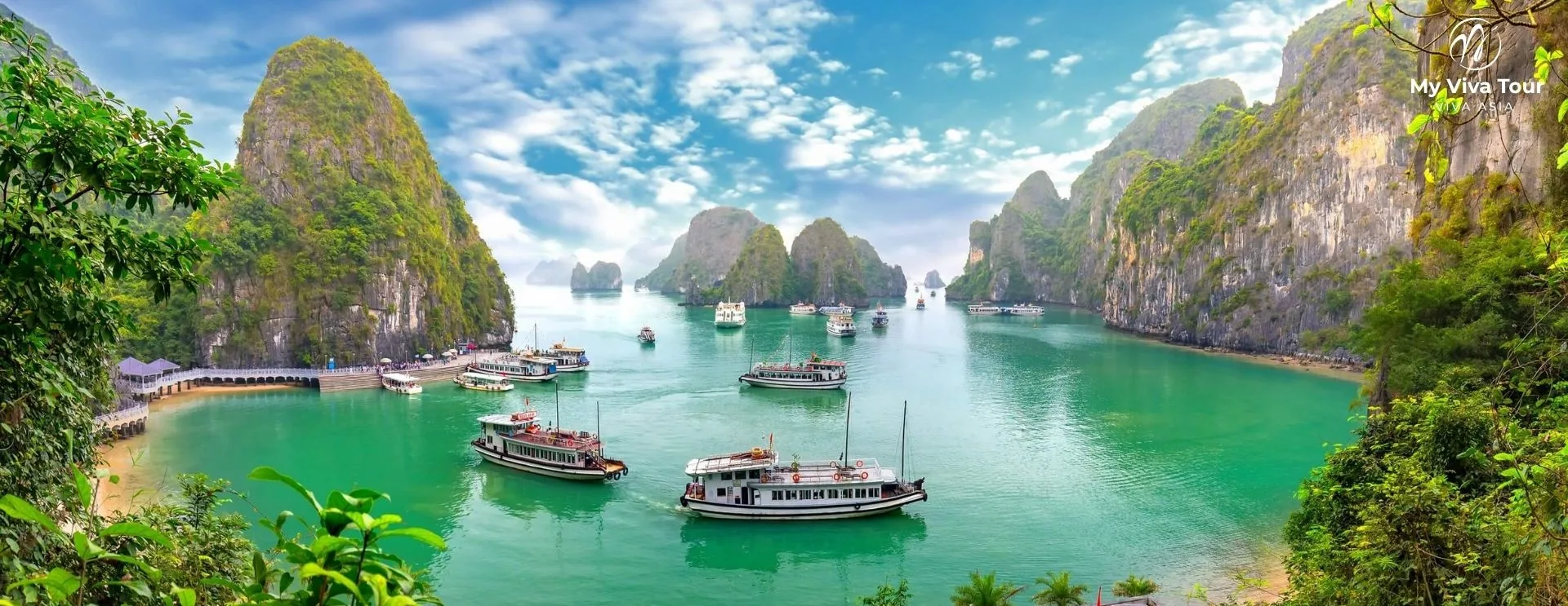 Wooden junk boats cruising between towering limestone karst islands on the emerald water of Ha Long Bay, a highlight of Vietnam private tours