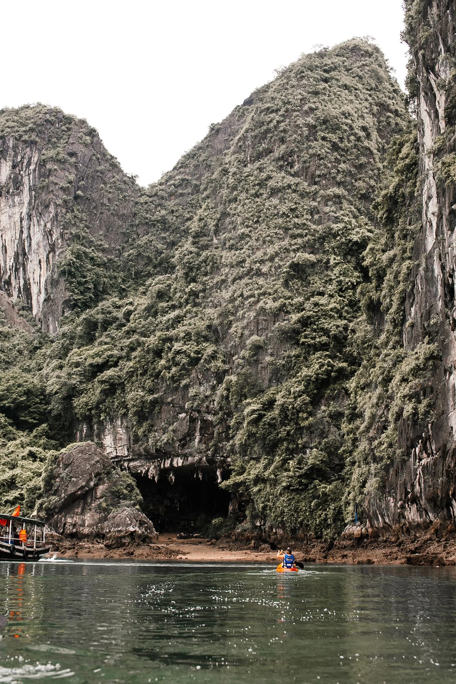 Kayaker paddling toward a limestone cave entrance in Ha Long Bay