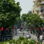Leafy Hanoi Old Quarter street busy with motorbikes and flags, Vietnam