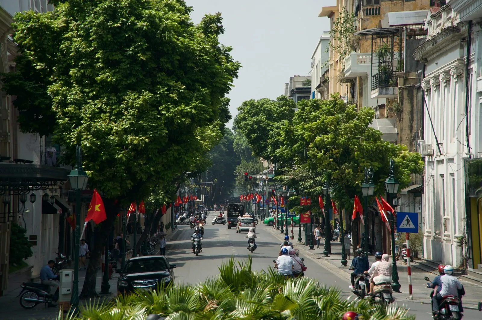 Leafy Hanoi Old Quarter street busy with motorbikes and flags, Vietnam