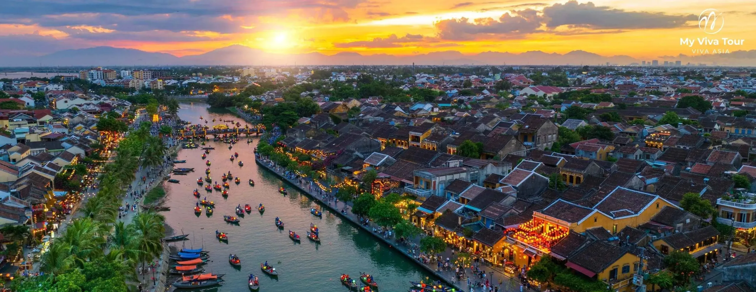 Aerial sunset view over Hoi An Ancient Town and the Thu Bon River lined with wooden boats, Vietnam