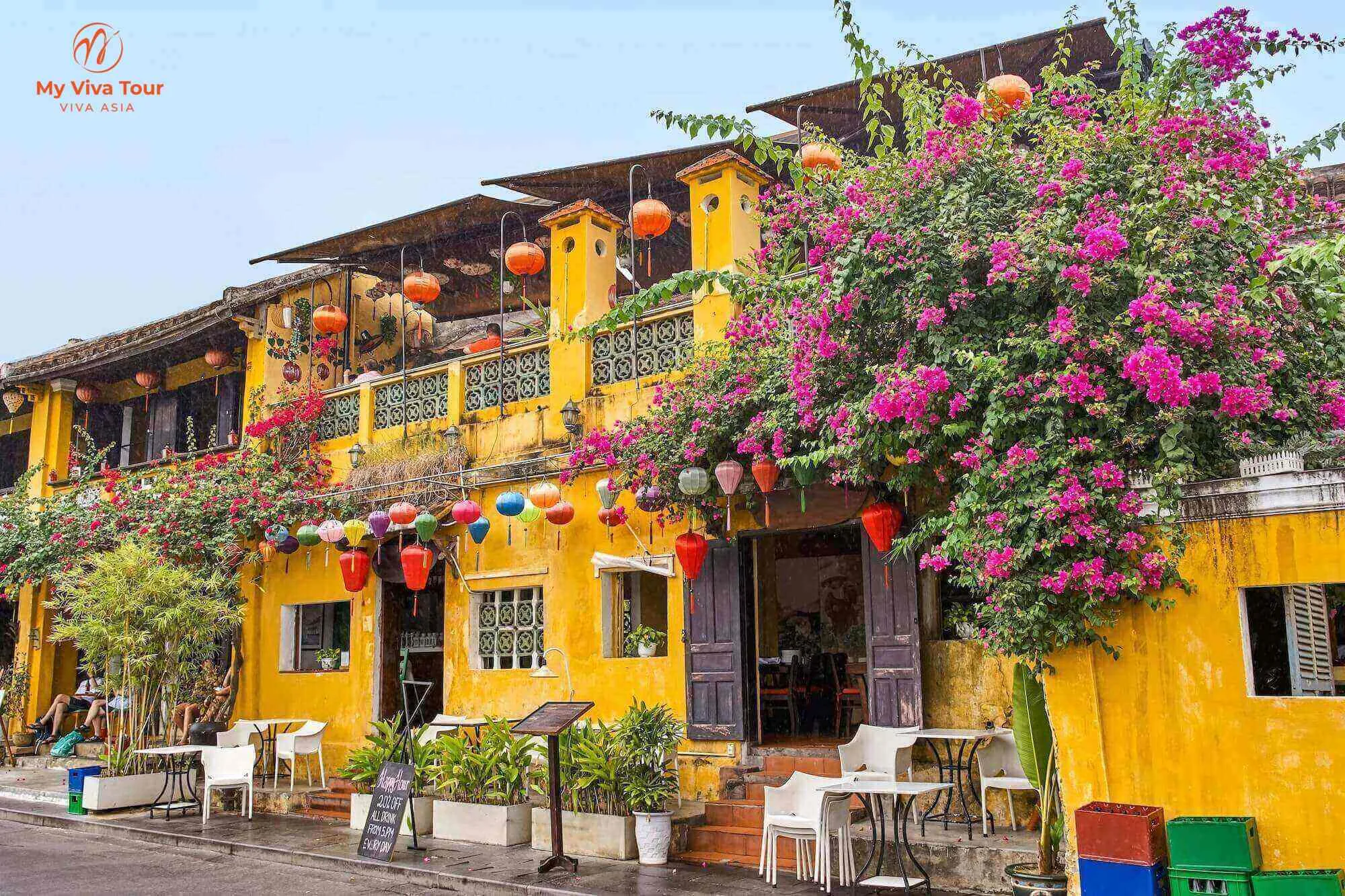 Historic mustard-yellow shophouse in Hoi An Ancient Town draped with colourful silk lanterns and pink bougainvillea