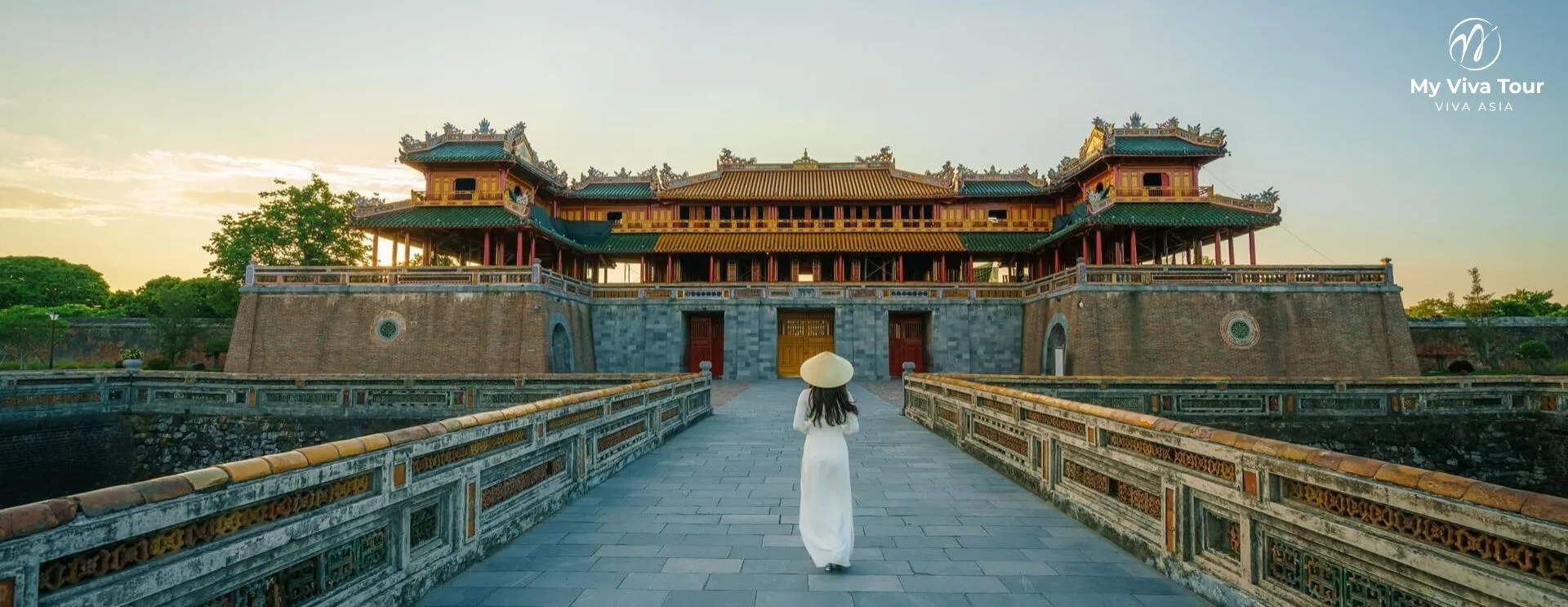 Woman in a white ao dai walking towards the Ngo Mon Gate of the Imperial Citadel at sunrise in Hue, Vietnam
