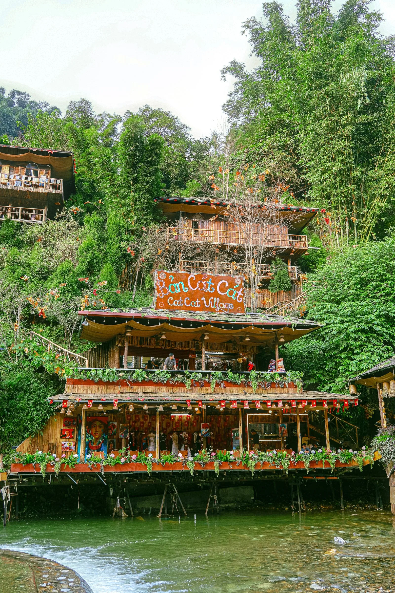 Wooden stilt houses and the Cat Cat Village sign beside a stream near Sa Pa town