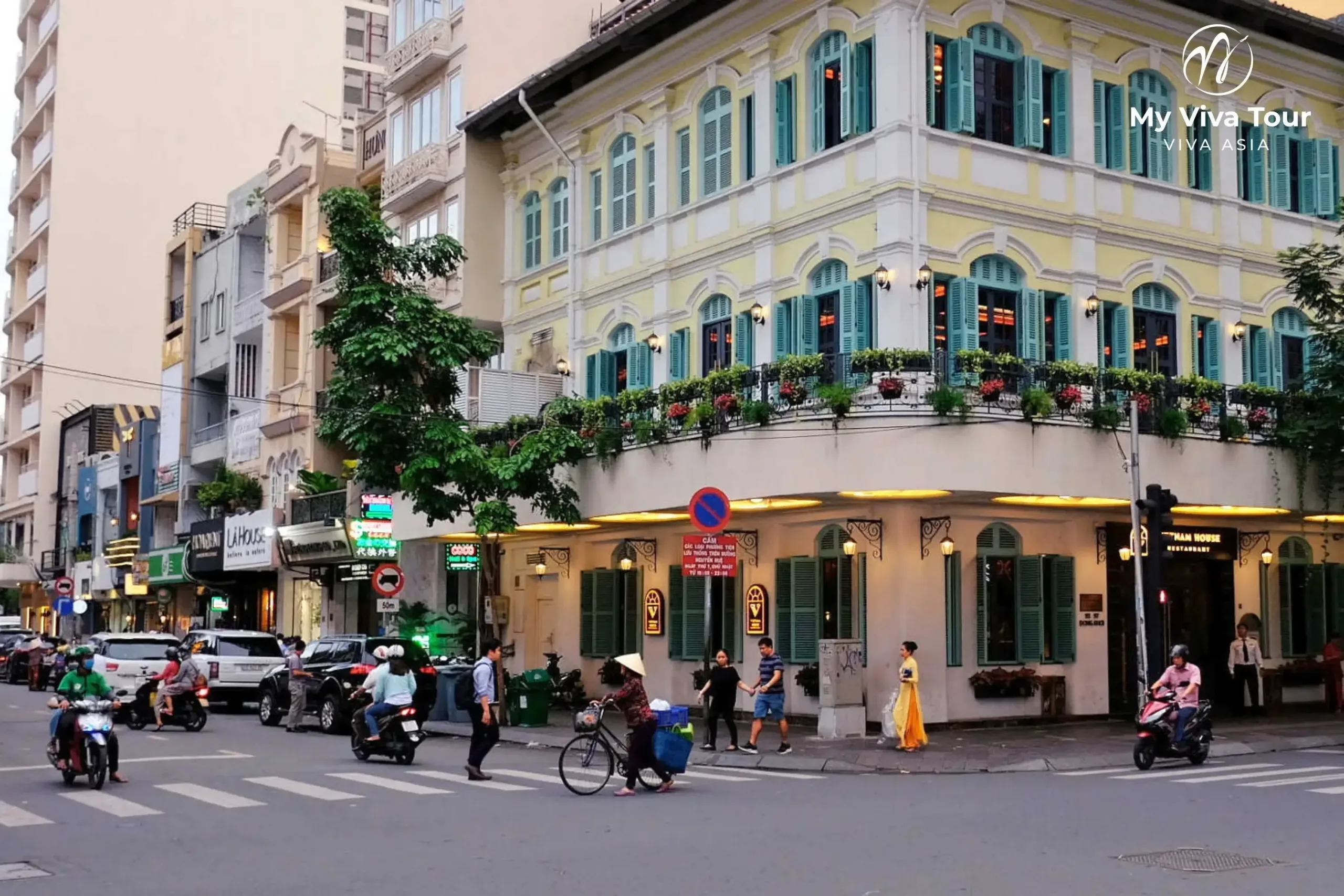 A calm Ho Chi Minh City street corner with taxis, motorbikes and pedestrians at a marked crossing