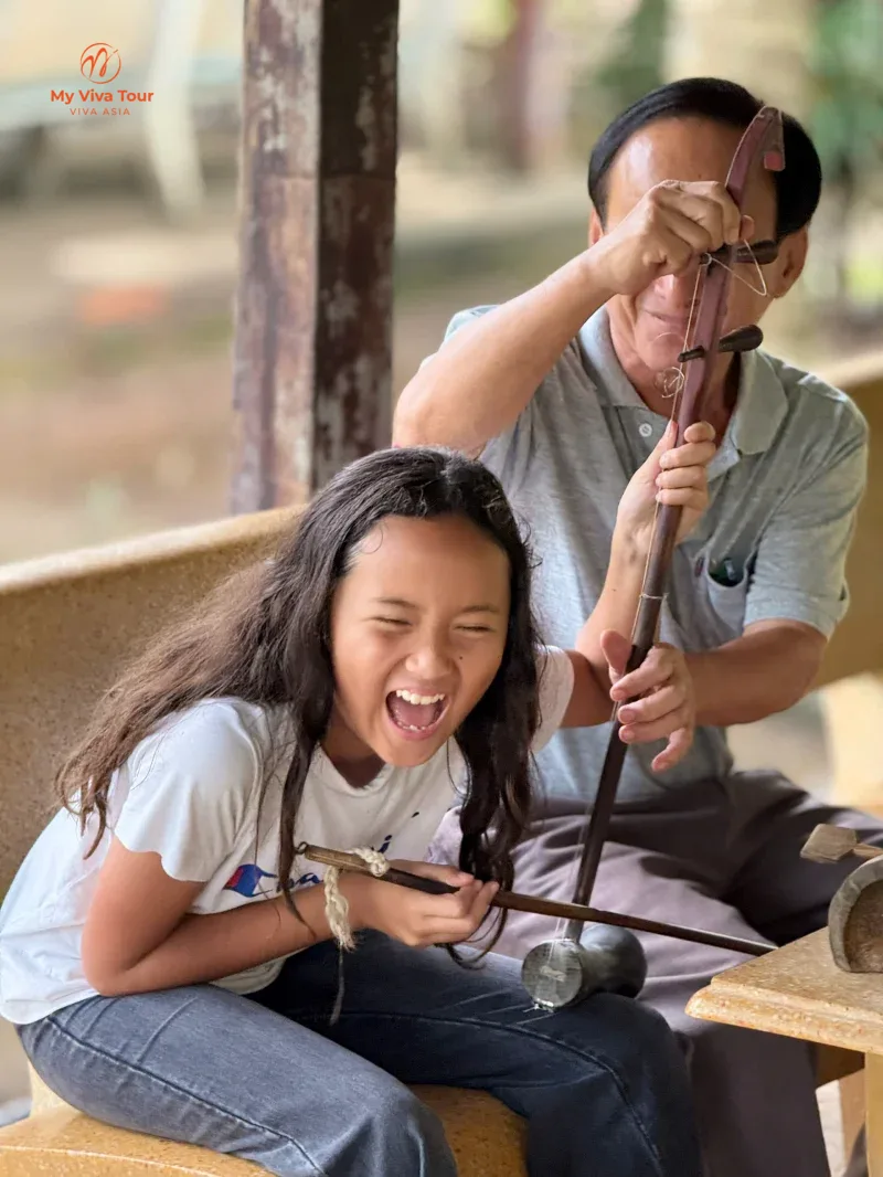 A member of Jerome's family trying a traditional Vietnamese instrument with a local musician