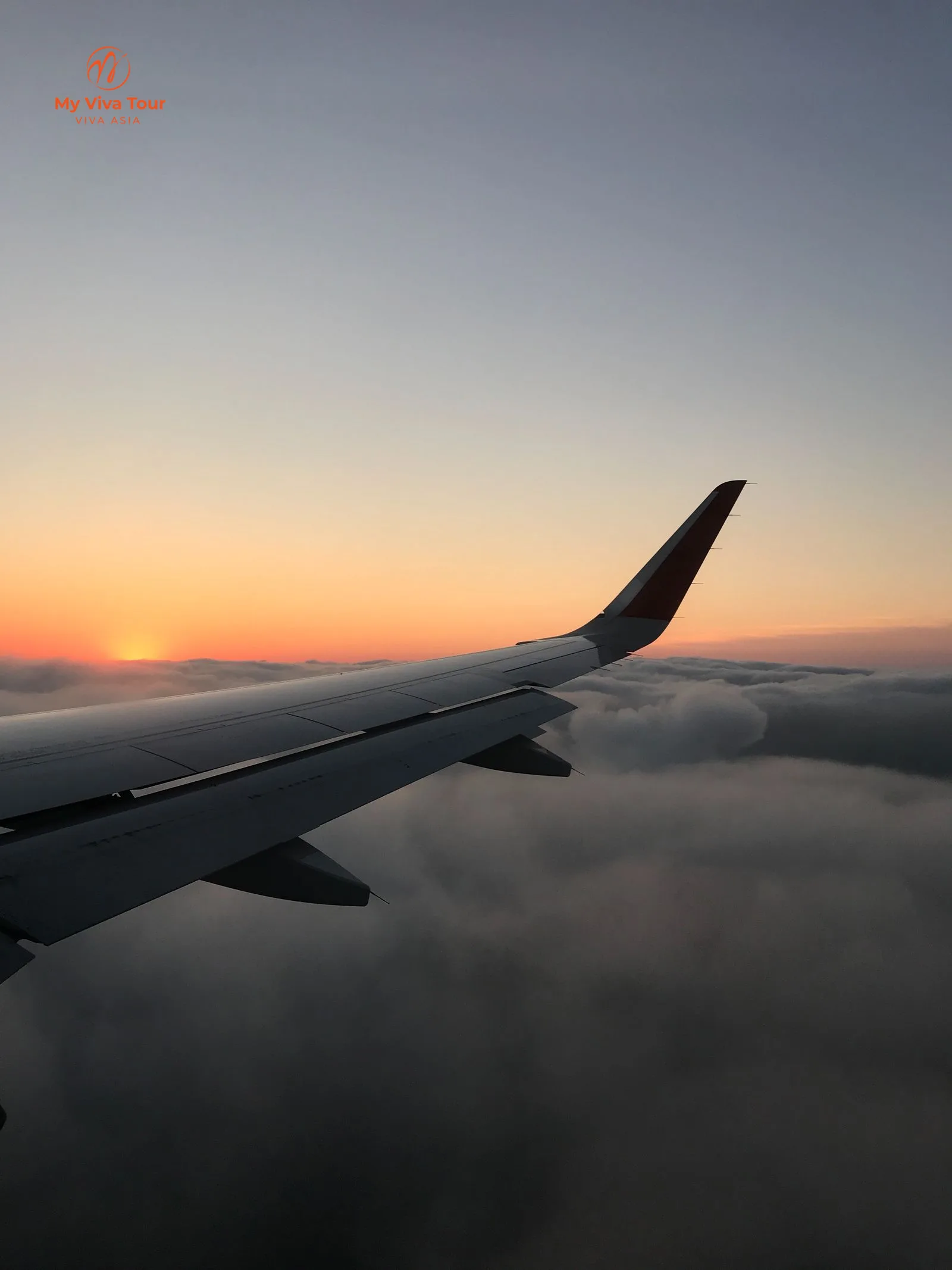 View from an airplane window of the wing above the clouds at sunset on a long-haul flight to Vietnam