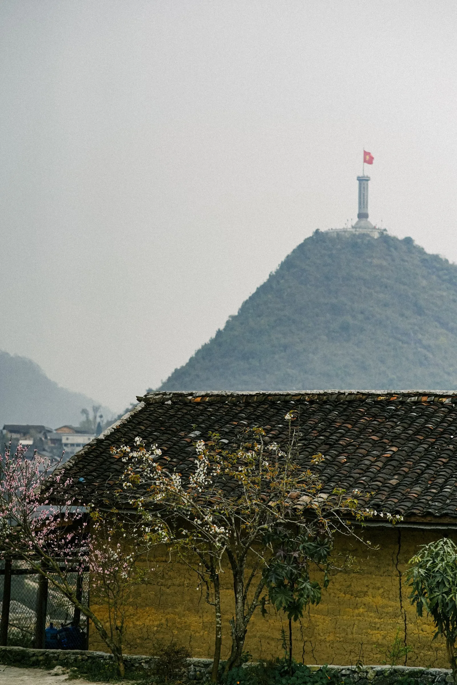 Lung Cu Flag Tower on a hilltop marking the northernmost point of Vietnam, above a tiled-roof village house