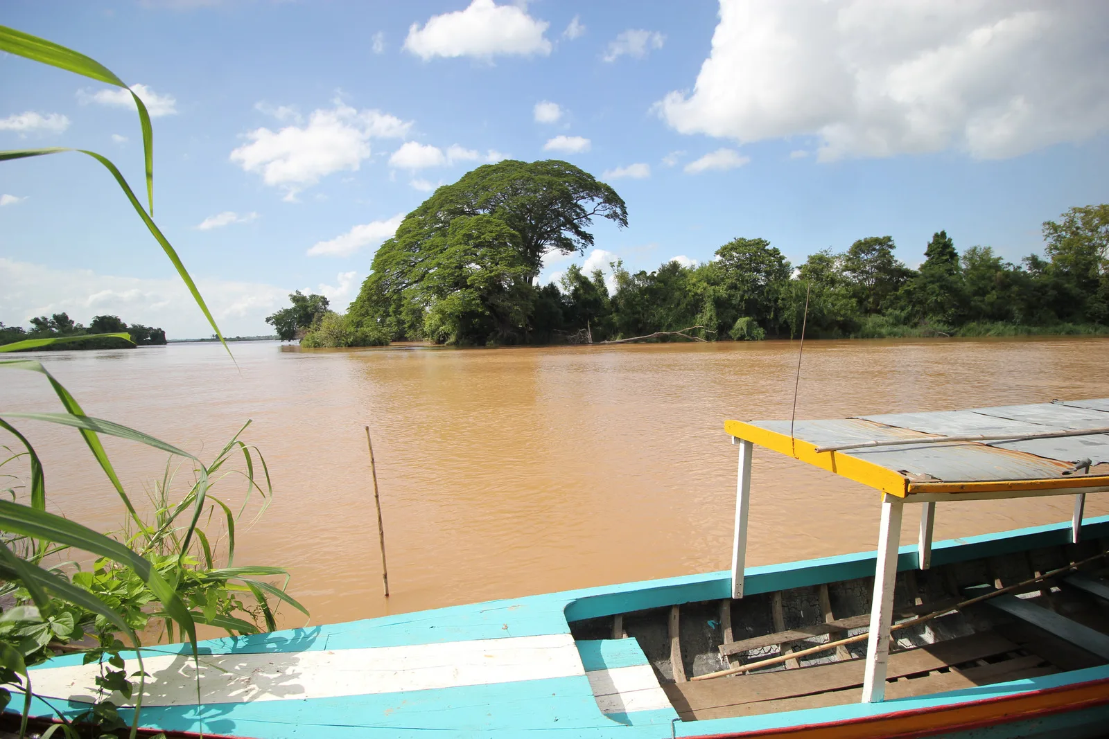 Wooden passenger boat moored on the Mekong River in southern Laos with a rain tree on a mid-river island
