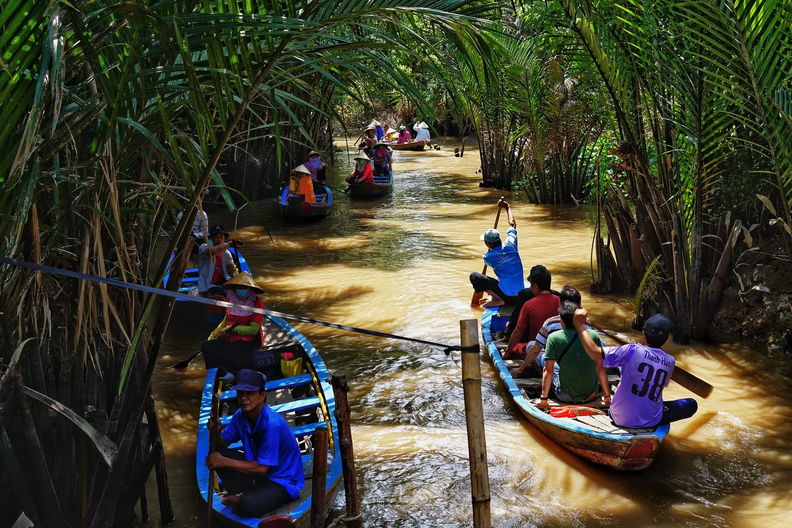 Visitors and local rowers in small wooden sampans on a narrow palm-shaded canal in the Mekong Delta