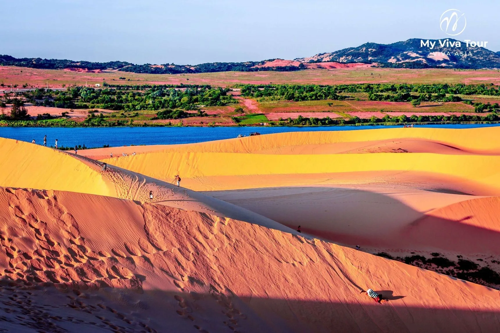 Red sand dunes beside a lake at Mui Ne under clear dry-season skies on Vietnam's south-central coast