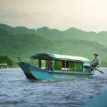 Phong Nha travel guide: a blue wooden tour boat marked Phong Nha Cave on the Son River below green karst hills