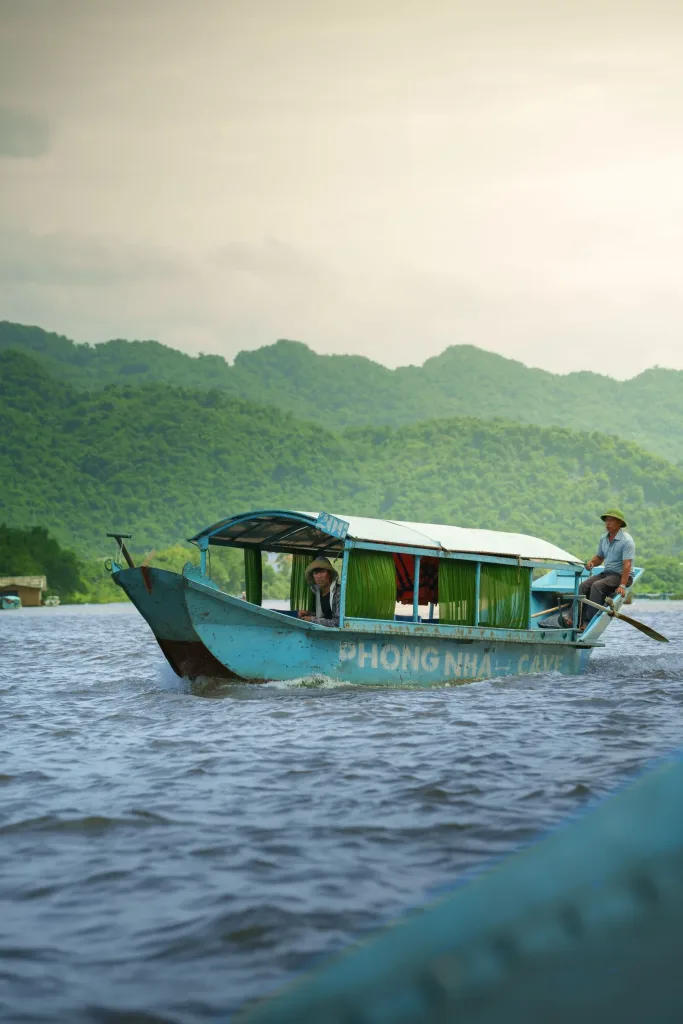 Phong Nha travel guide: a blue wooden tour boat marked Phong Nha Cave on the Son River below green karst hills
