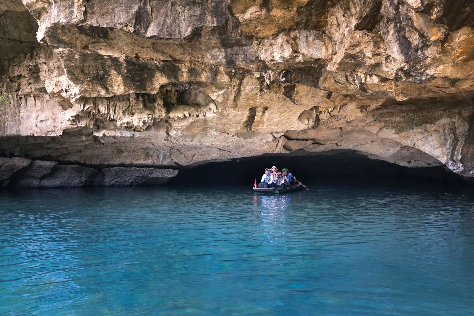 Small tour boat carrying visitors into the mouth of Phong Nha Cave over turquoise water