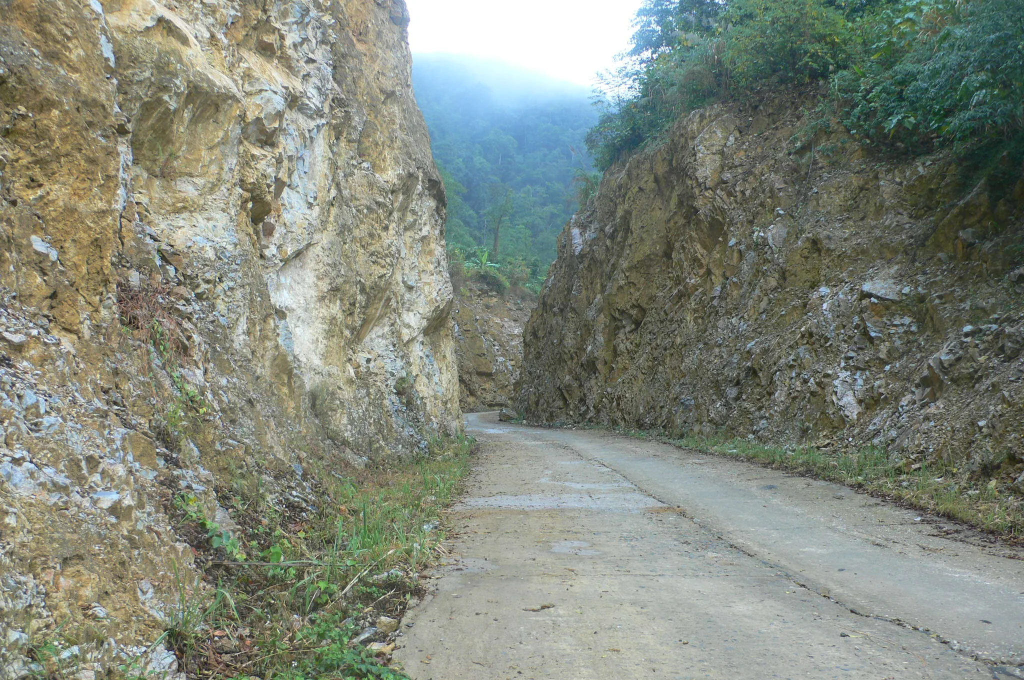 Narrow concrete road cut between limestone rock walls leading into the remote Son Ba Muoi area of Pu Luong