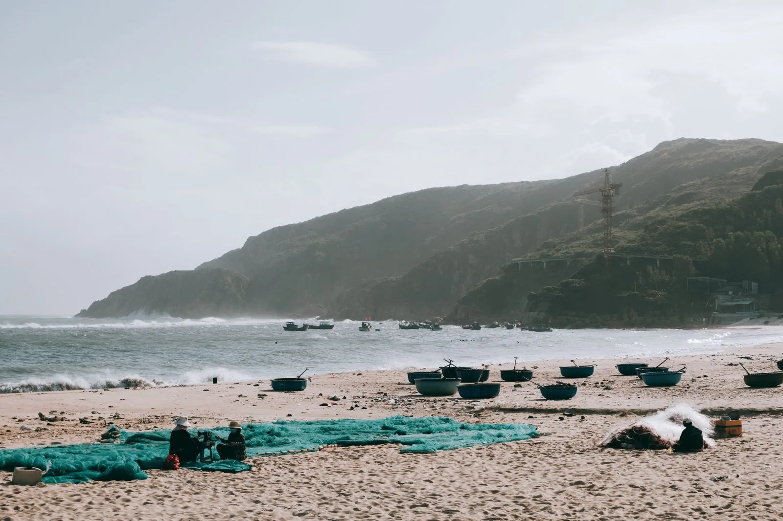 Round basket boats on a sandy Quy Nhon beach with cliffs and fishing boats offshore