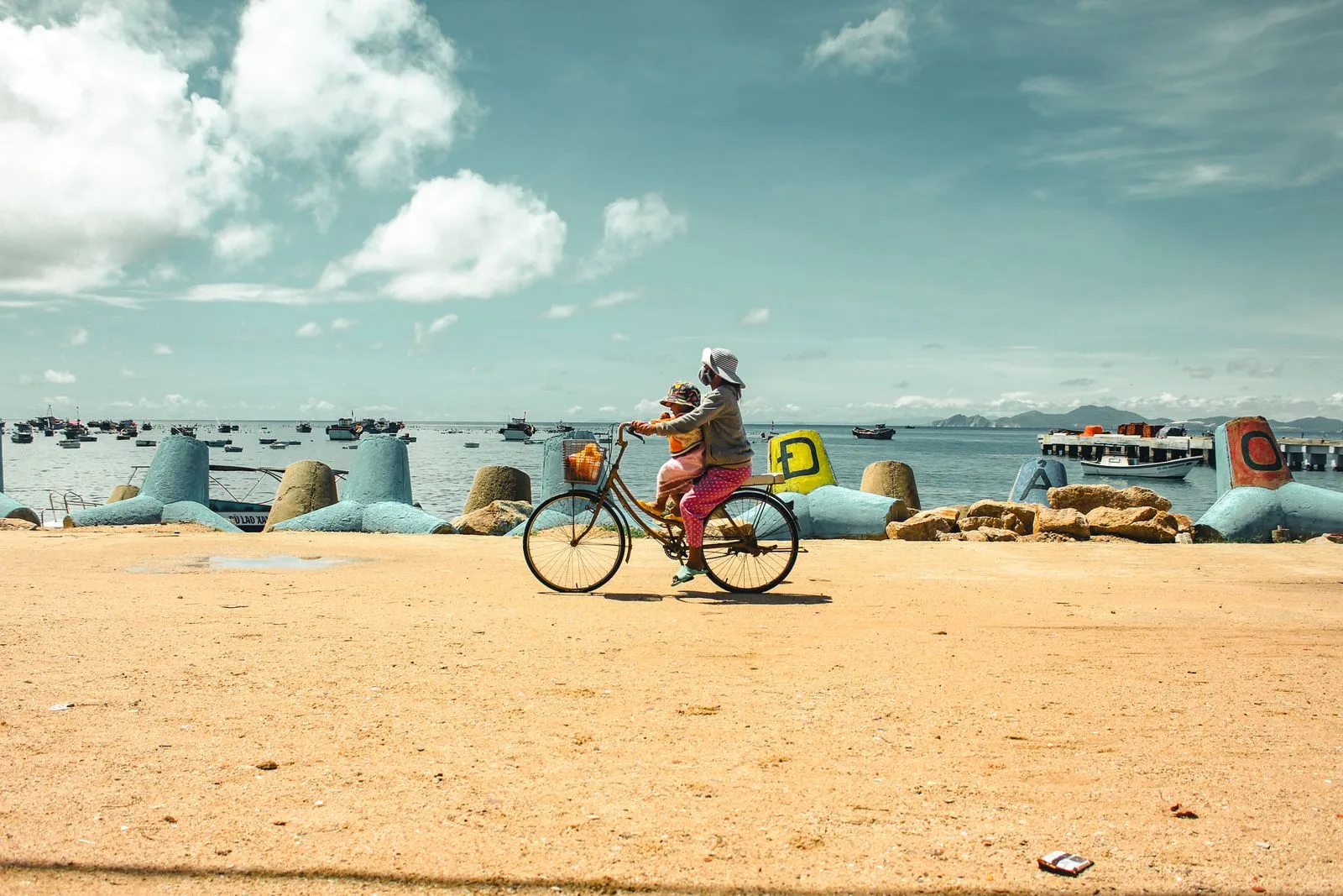 Woman cycling with a child along a Quy Nhon waterfront lined with fishing boats