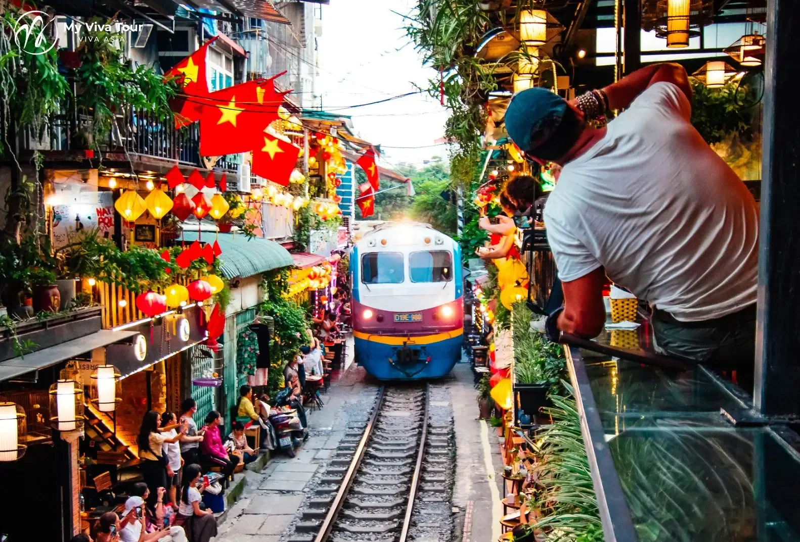 Travellers watching the train pass along Hanoi Train Street at dusk