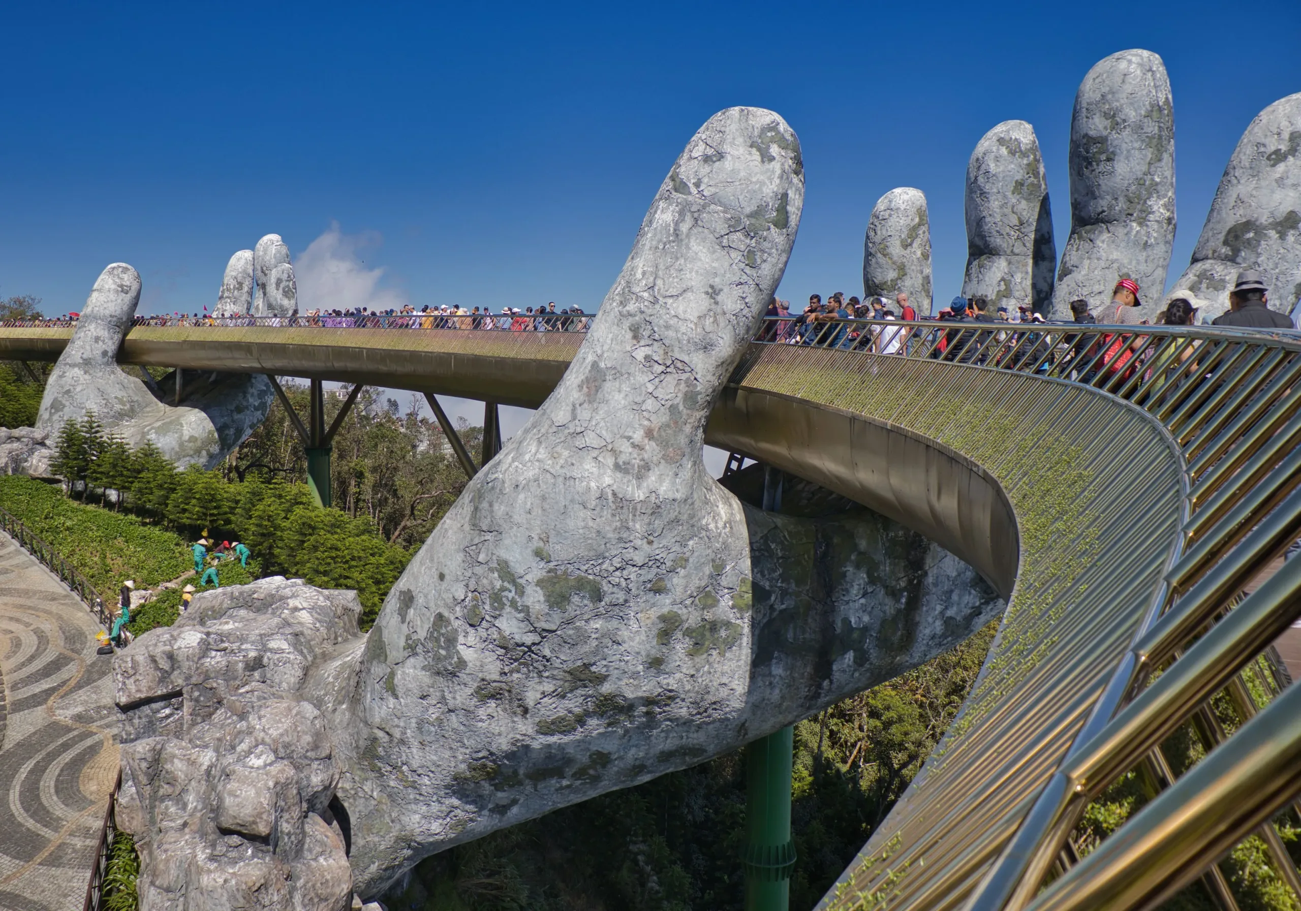 Visitors crossing the Golden Bridge held by giant stone hands at Ba Na Hills