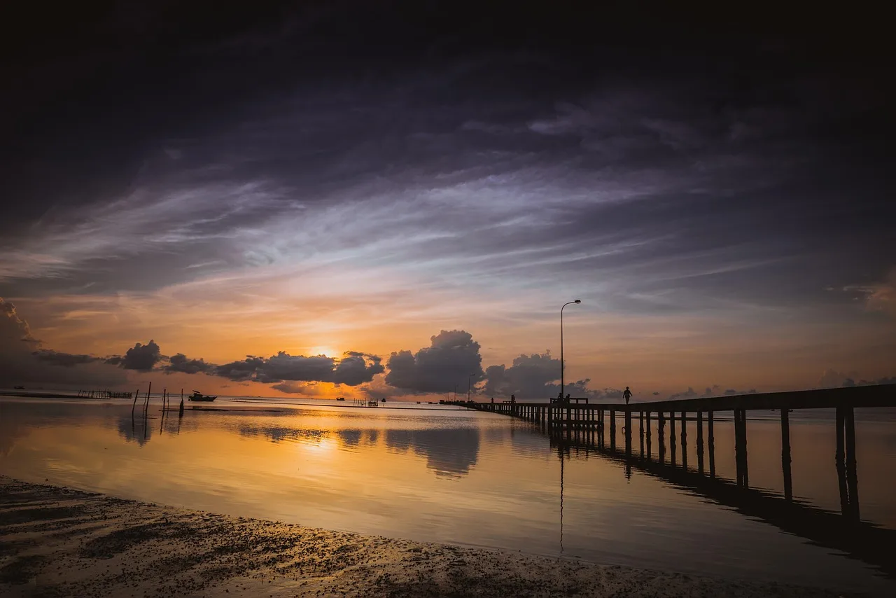 Long wooden jetty reaching over calm water at Ham Ninh fishing village on Phu Quoc under a golden dawn sky