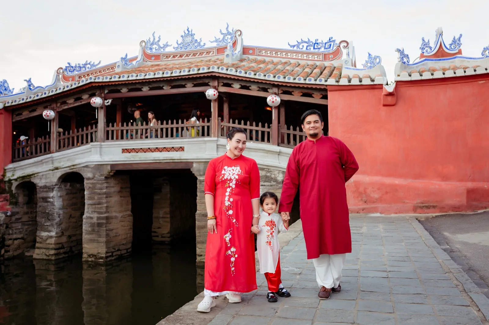 Family in red ao dai standing in front of the Japanese Covered Bridge in Hoi An