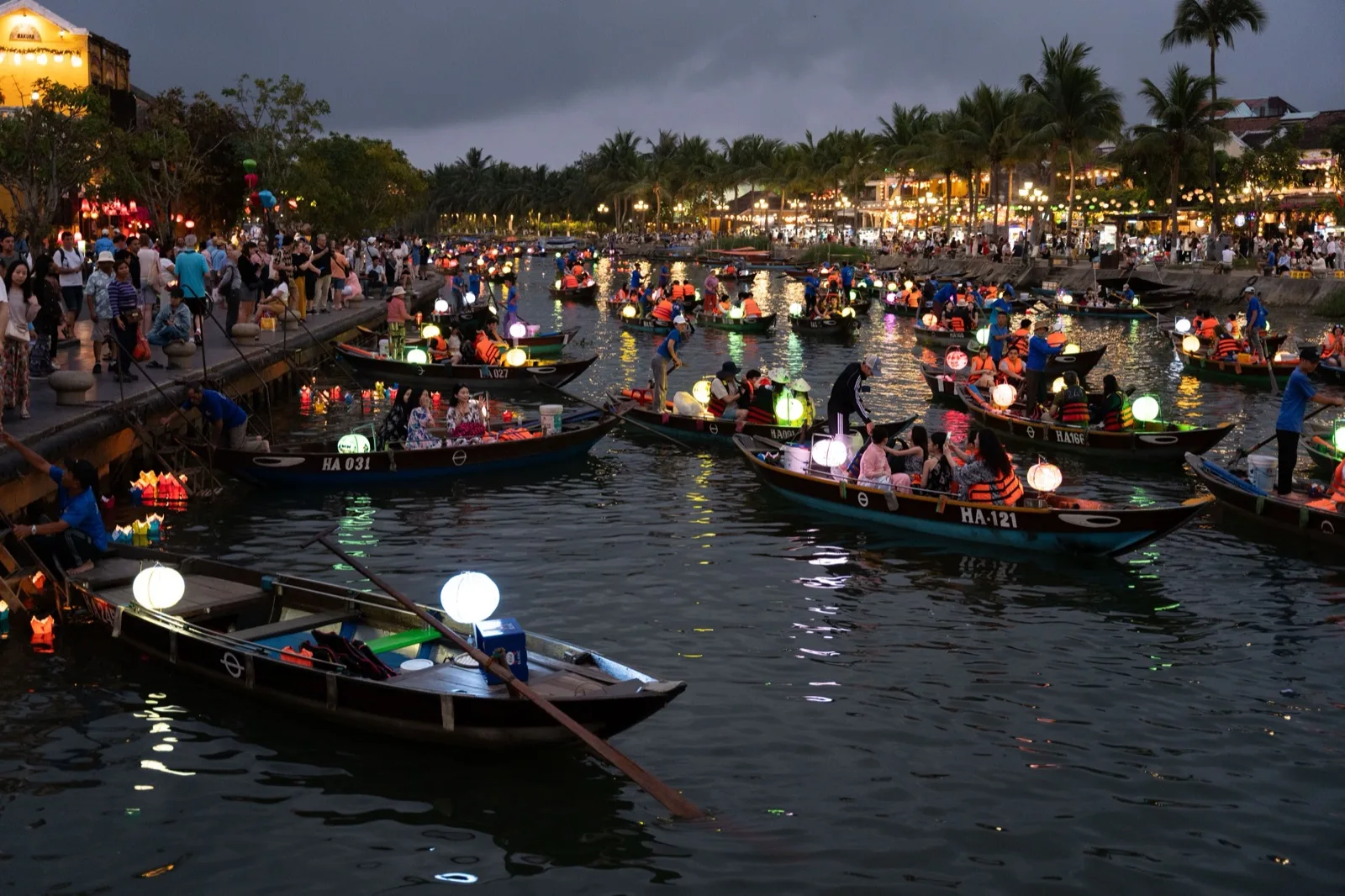 Wooden boats carrying glowing lanterns on the river in Hoi An at dusk