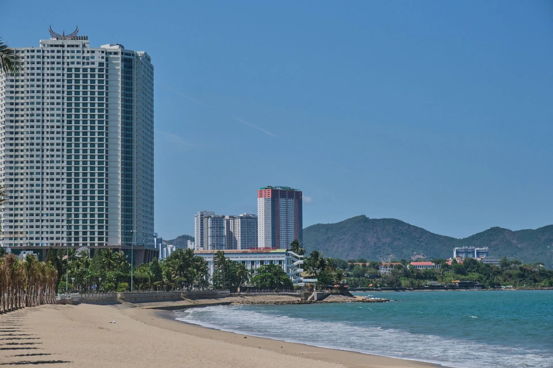 Nha Trang travel guide: high-rise hotels and palm trees along the sandy curve of Nha Trang beach with green hills behind