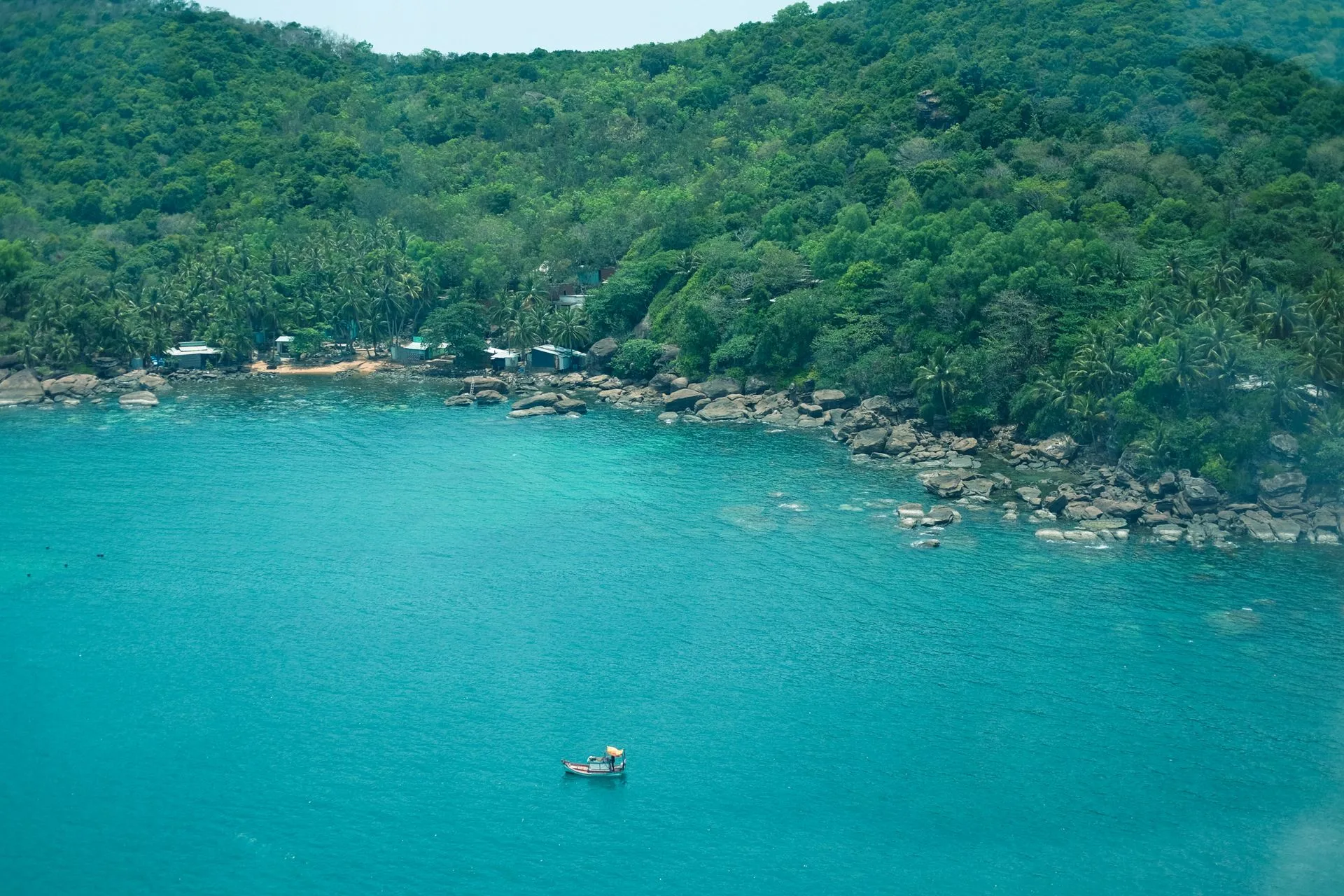Forested Phu Quoc coastline meeting clear turquoise water with a single fishing boat offshore