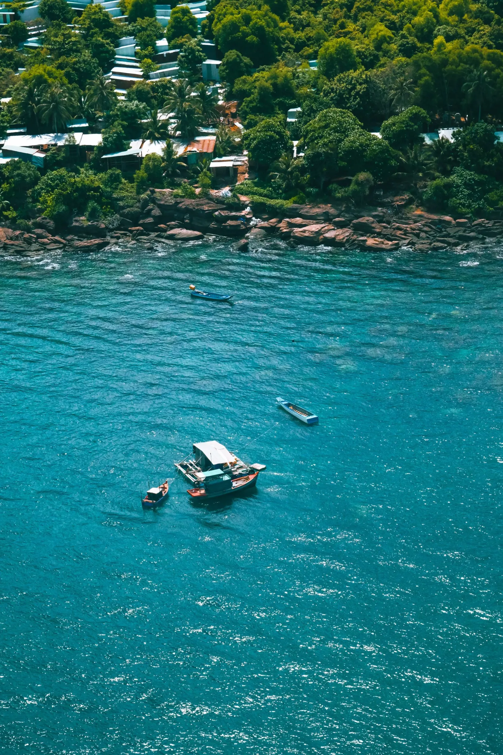 Tin-roofed fishing village above the rocks on Phu Quoc with wooden boats moored in turquoise water