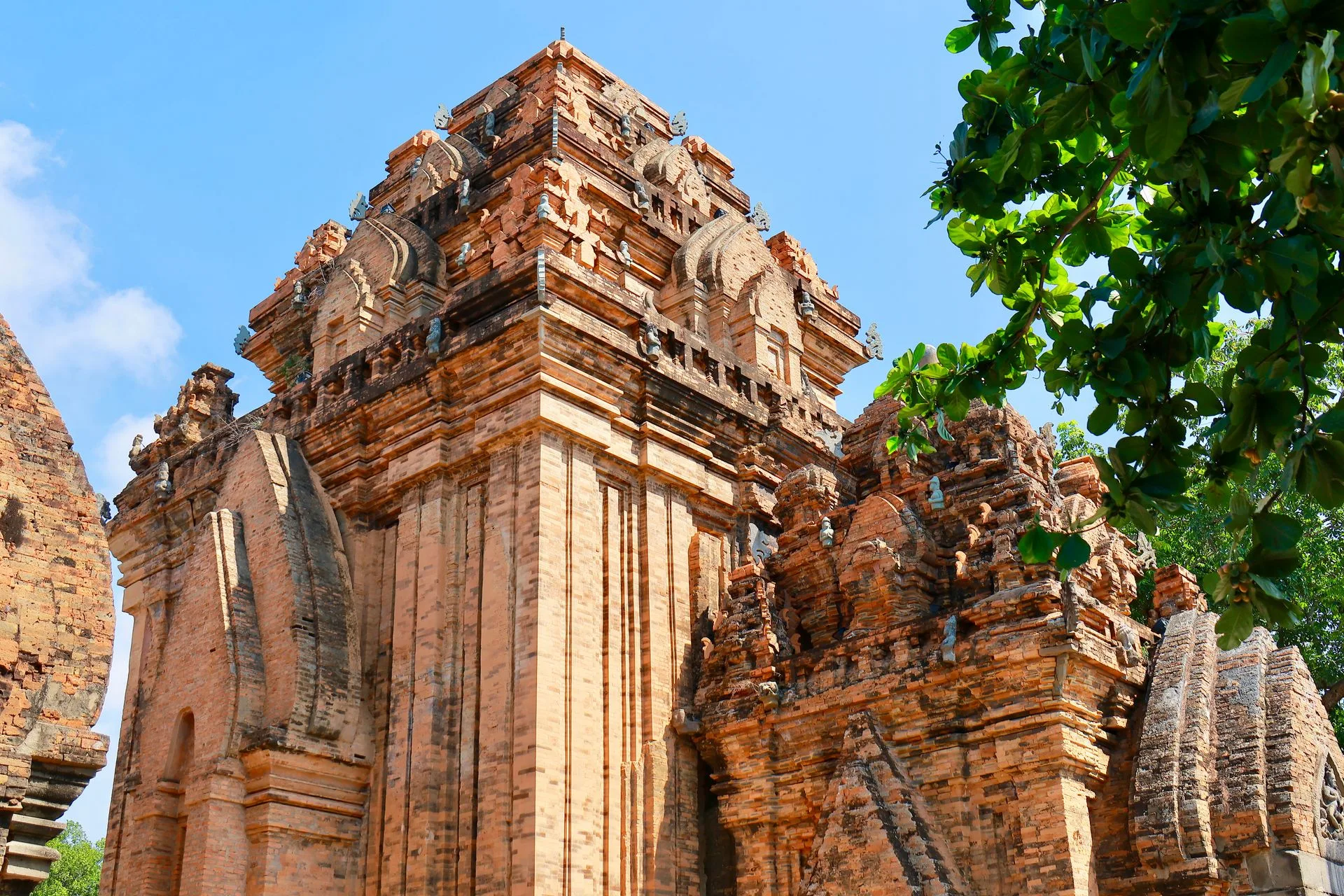 Red brick Cham towers of Po Nagar in Nha Trang, with tiered pyramidal roofs and carved stone figures against a blue sky