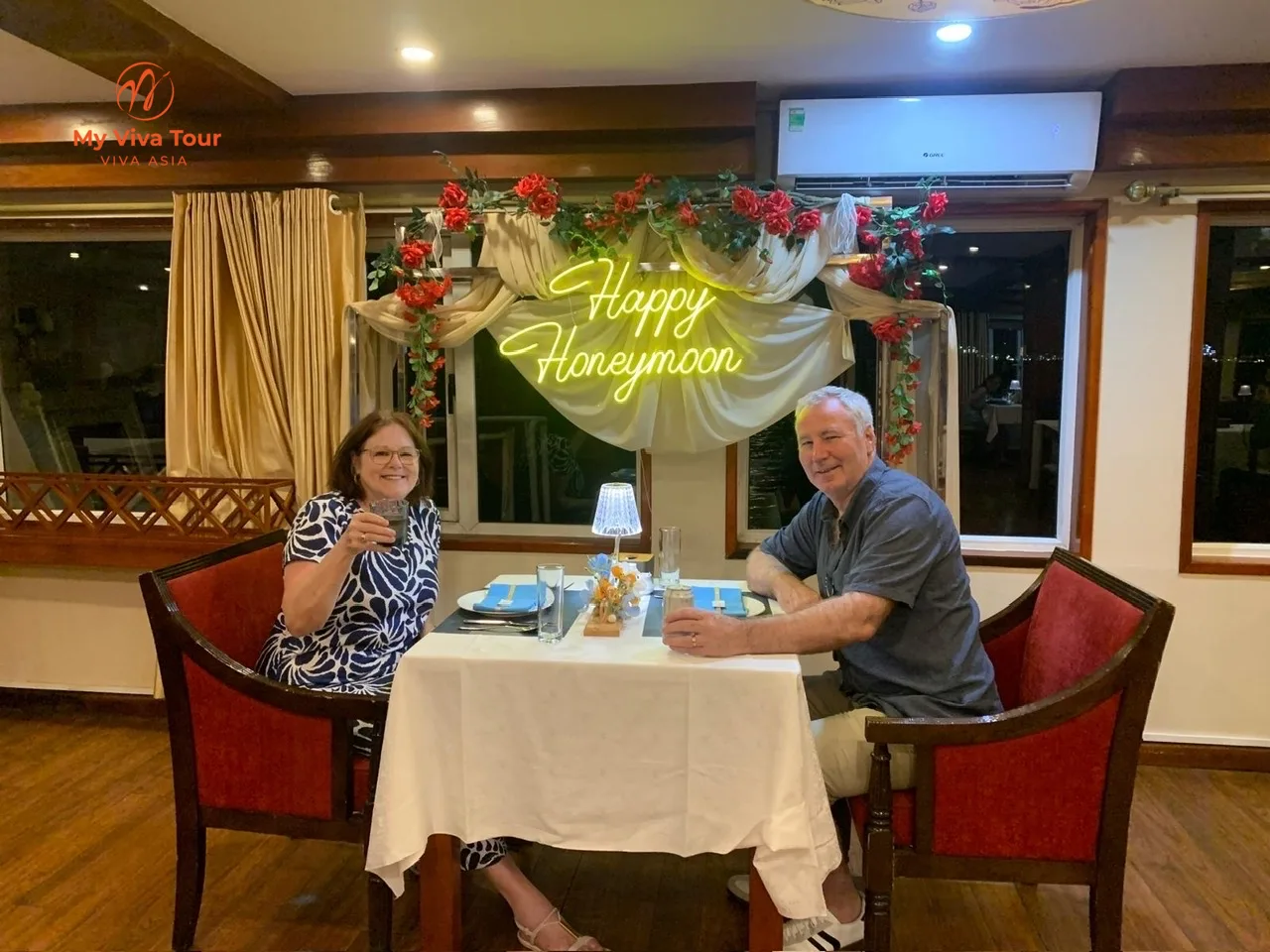 Two travellers raising a glass at a dinner table in a cruise dining room during the Ha Long Bay overnight