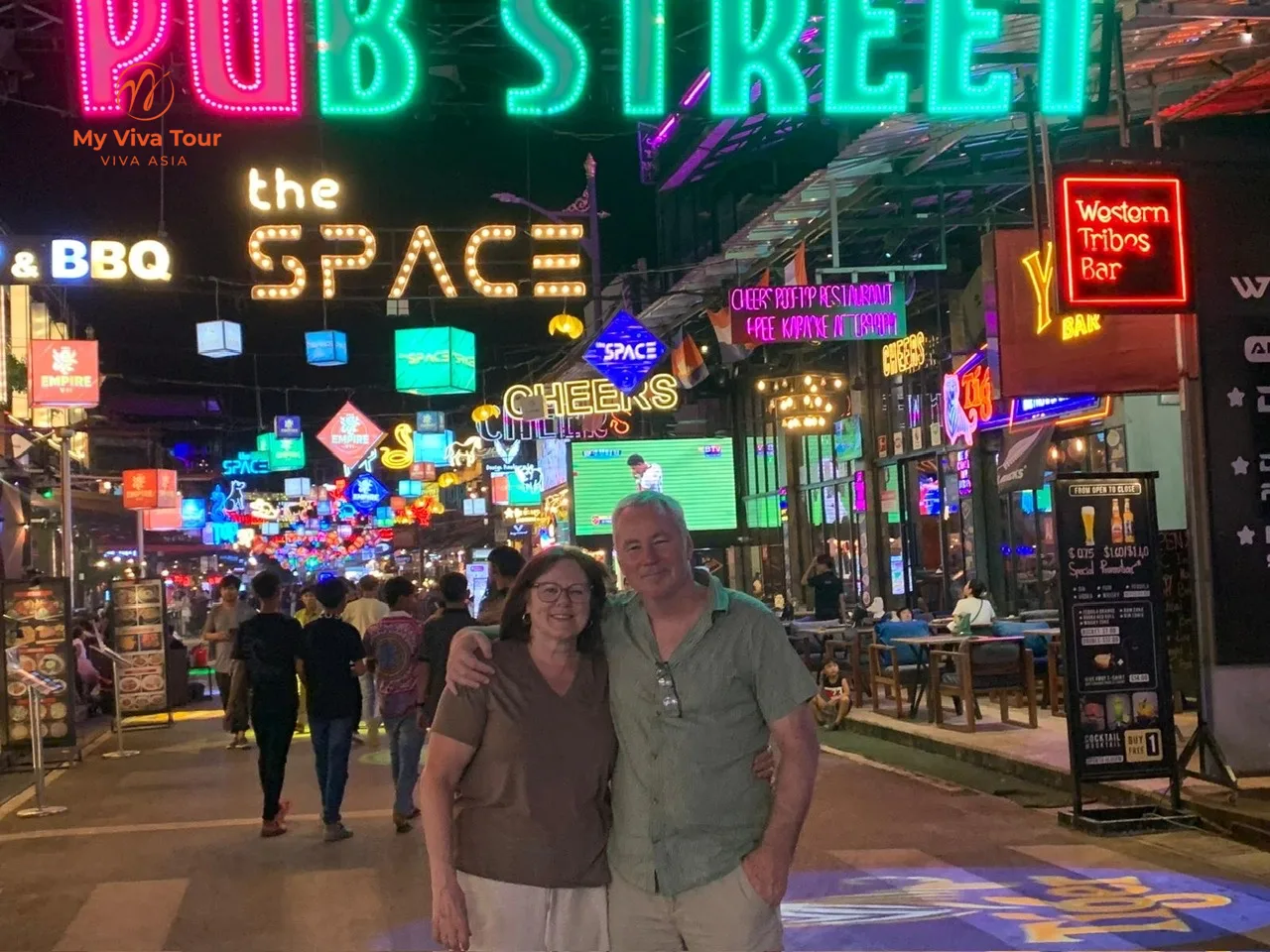 Carmen and her travel companion under the neon Pub Street sign in Siem Reap at night