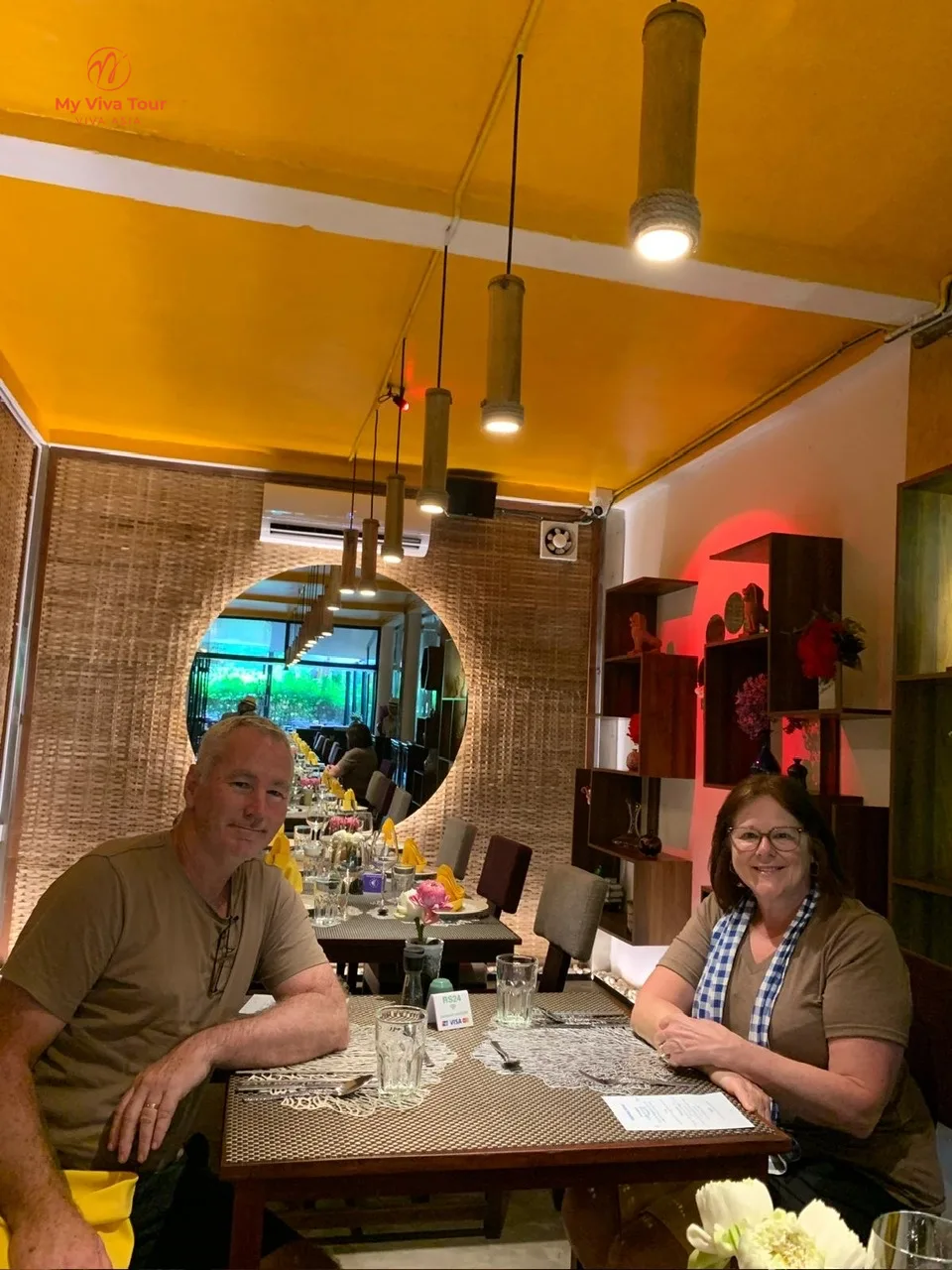 Two travellers at a restaurant table with a yellow ceiling and round mirror during a lunch stop