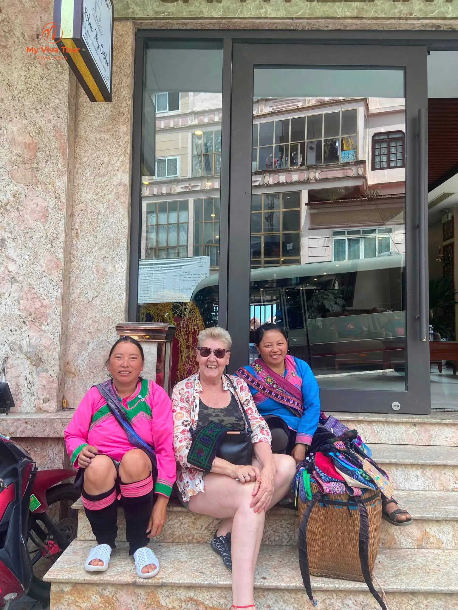 Missy sitting on hotel steps in Sapa between two local women in traditional embroidered dress