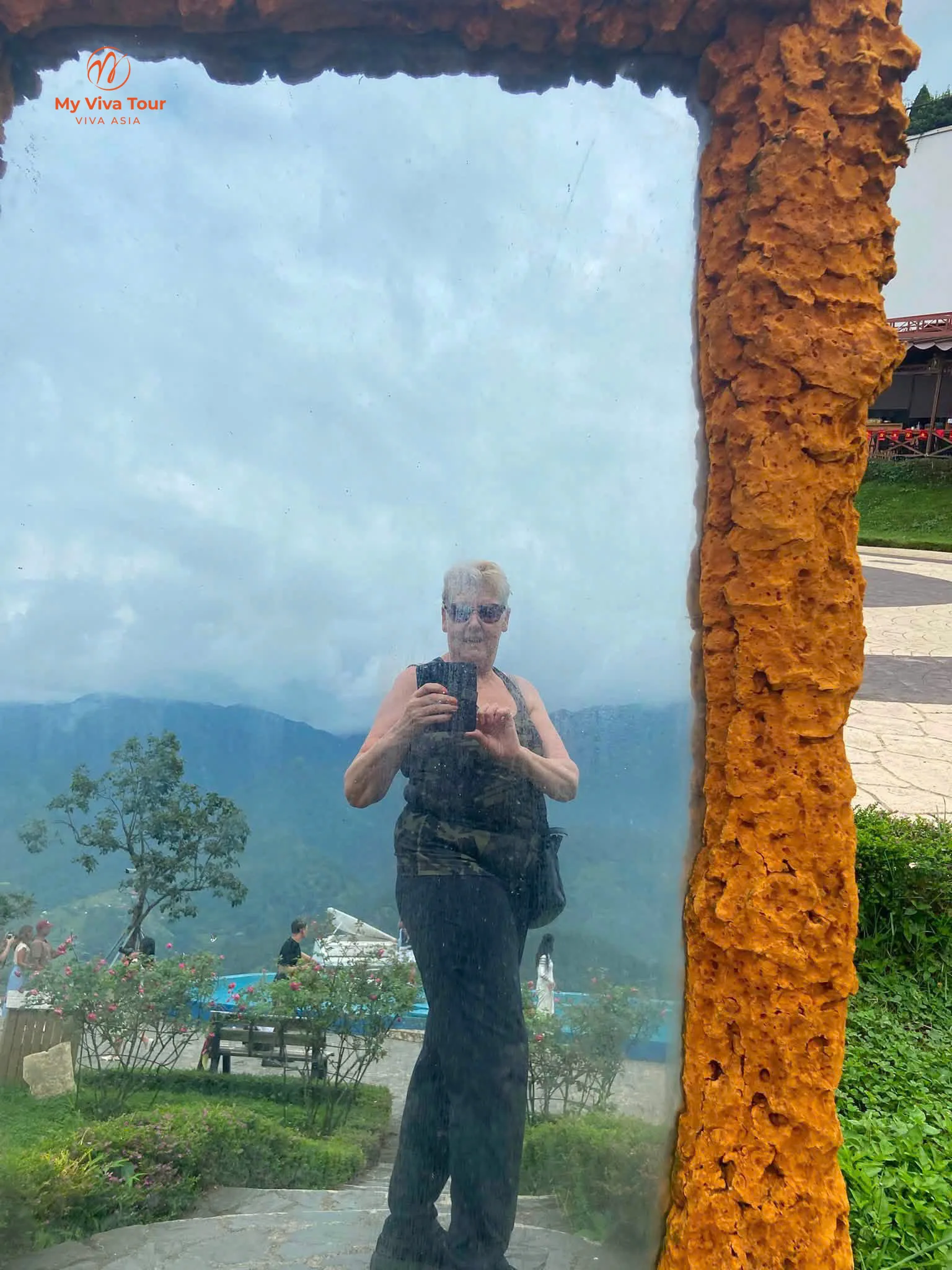 Missy taking a selfie in a framed mirror at a Sapa viewpoint, mountains and cloud behind