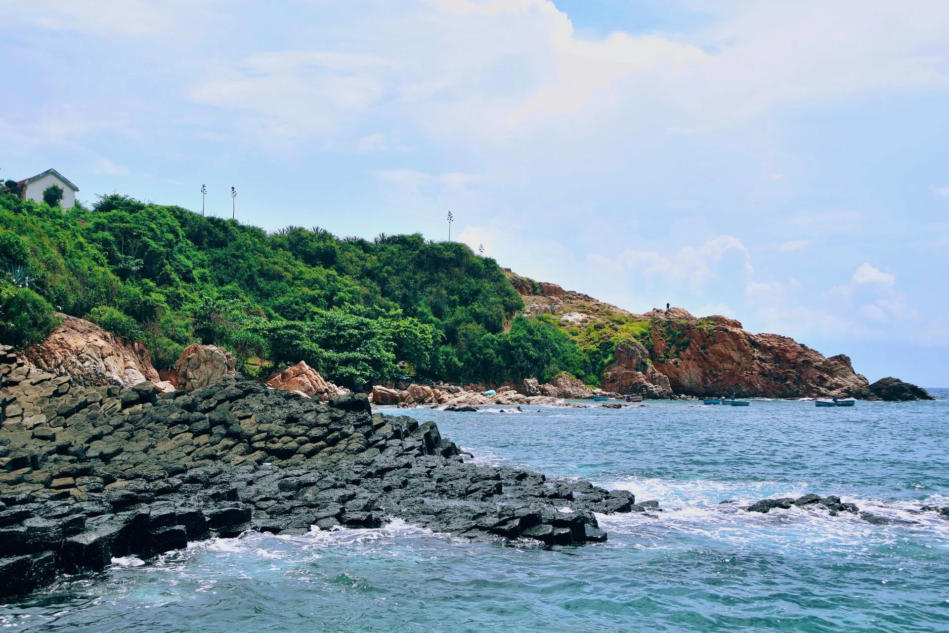 Basalt column shore at Ganh Da Dia with green headland and fishing boats beyond